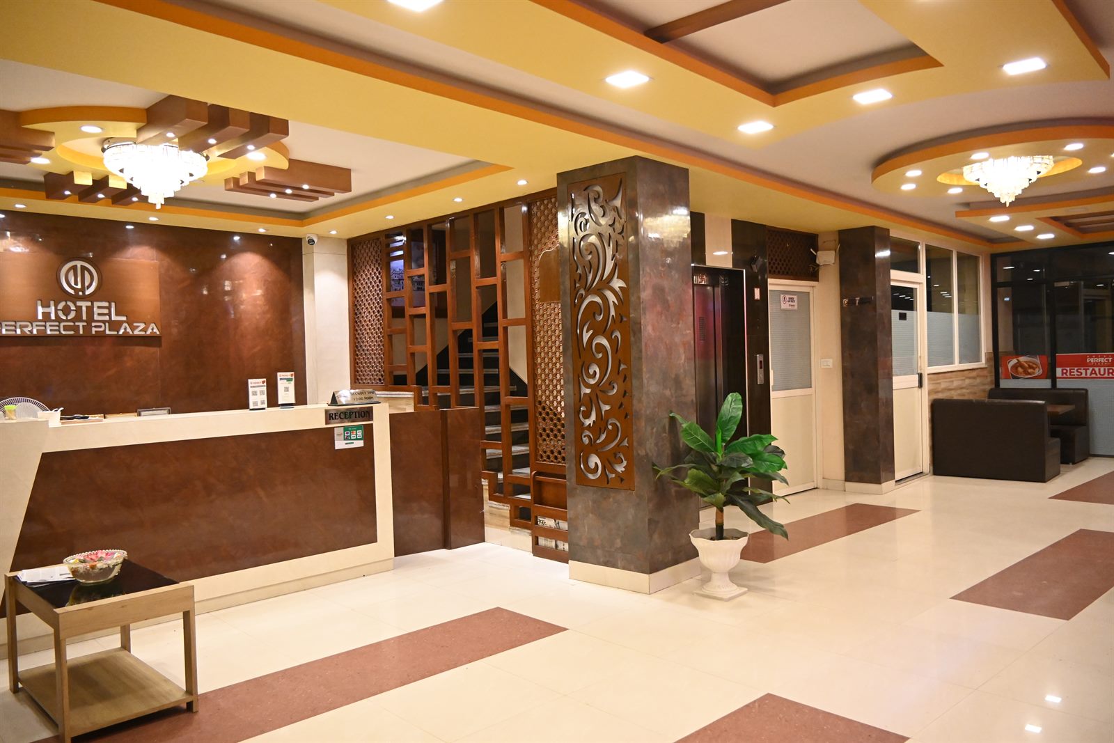 The reception and lobby at Hotel Perfect Plaza, with the hotel's sign, a decorative wooden screen and the lift