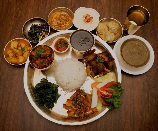 A Nepali thali on a brass plate: rice, dal, a meat curry, greens, potatoes, pickles and momos