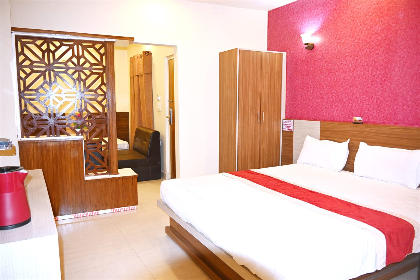 The Executive Room, with a bed set against a deep pink accent wall and a carved wooden screen